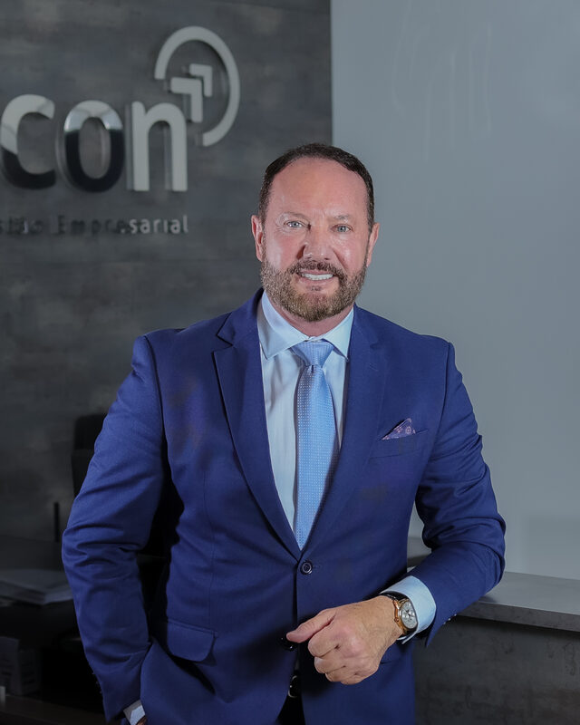 Nildo Pedrotti, sócio-fundador da Recon, de terno azul, diante do letreiro da empresa